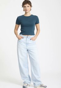 T-shirt corta color verde acqua realizzata in cotone, abbinata a jeans a gamba larga azzurri chiari, con vita alta e chiusura frontale con un solo bottone.