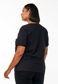 Juoda trumpomis rankovėmis t-shirt, pagaminta iš medvilnės, su apvaliu iškirpimu ir laisvu siluetu. Derinama su tamsiomis džinsomis, pateikta šiek tiek iš šono.