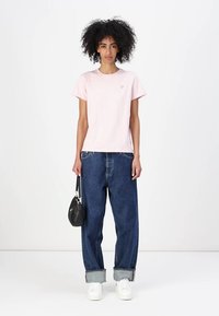 Tricou din bumbac de culoare roz deschis, cu mâneci scurte și un mic logo pe piept, asociat cu blugi albaștri largi din denim și adidași albi.