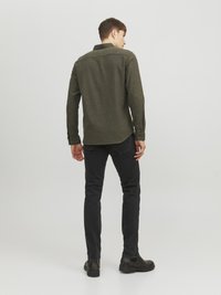 Camisa de manga larga color verde oscuro, de corte casual, con botones contrastantes y dobladillo recto, combinada con jeans negros ajustados y botas negras.