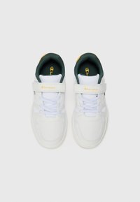 Baskets blanches avec des accents verts et jaunes, présentant une tige synthétique lisse, un bout rond, un laçage à l'avant et une sangle Velcro.