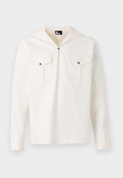Chemise à manches longues crème avec capuche, fermeture à boutons sur le devant, deux poches poitrine avec rabats et texture de tissu lisse.