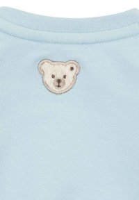 Prenda azul claro con una textura suave, que presenta un bordado de la cara de un oso en crema en la parte posterior, realzado por costuras beige.