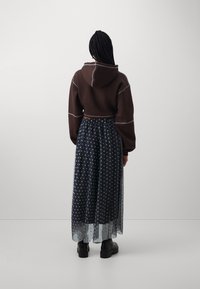 Brun cropped hoodie med hvid syning, parret med en lang sort tylskørt med prikker og sorte platformstøvler.