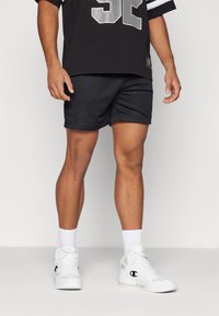 Pantalones cortos deportivos negros hechos de tela de malla, con un corte suelto. Combinados con una camiseta negra y zapatillas blancas de caña alta con acentos de logo.