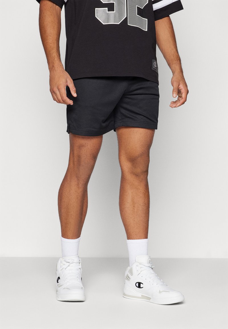 Pantalones cortos deportivos negros hechos de tela de malla, con un corte suelto. Combinados con una camiseta negra y zapatillas blancas de caña alta con acentos de logo.