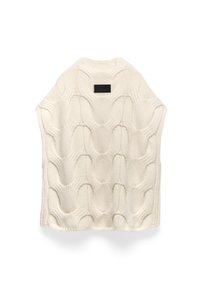 Sweter bez rękawów w kolorze kremowym, z teksturowanym wzorem wypukłych ovalnych kształtów. Okrągły dekolt i prostokątna czarna metka z tyłu.
