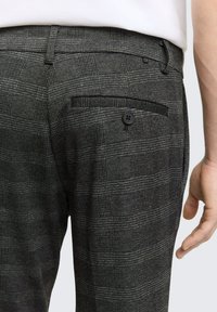 Szare spodnie w kratę z tylną kieszenią z czarnym guzikiem. Tkanina ma teksturowane wykończenie z delikatnym wzorem w kratę.