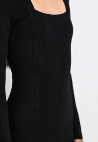 Black knitted dress featuring a square neckline, ribbed accents, vertical stripes, and fine texture with detailed patterns.