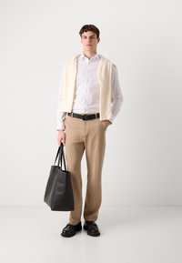Lys lange ermer skjorte, kremfarget genser lagt over skuldrene, beige bukser, svart belte, svart lær tote bag og svarte sko.