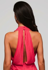 Robe halter rose avec un dos dénudé, présentant un design froncé et deux boutons au cou. Texture lisse et tissu léger.