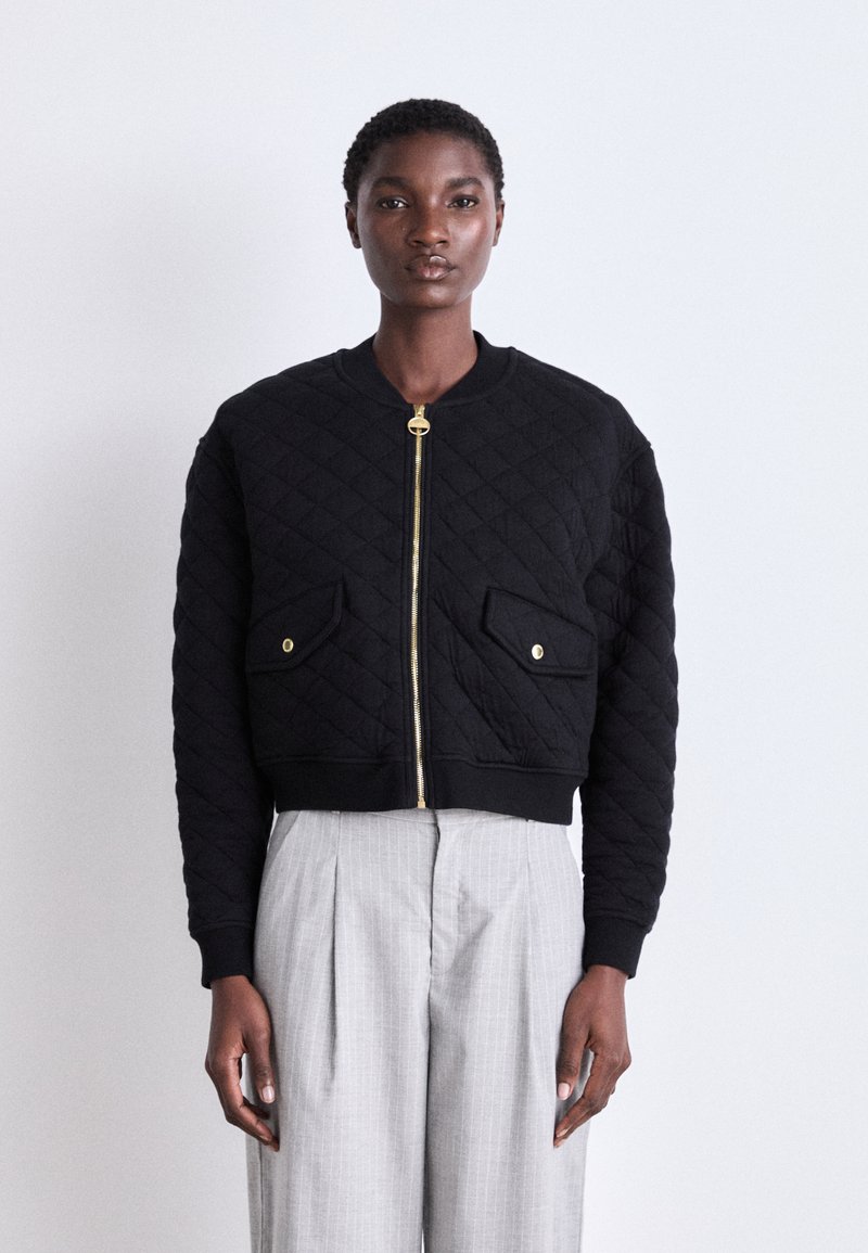 Jaqueta bomber preta acolchoada com fecho de correr, detalhes em dourado e dois bolsos frontais. Design cropped com punhos e bainha canelados.