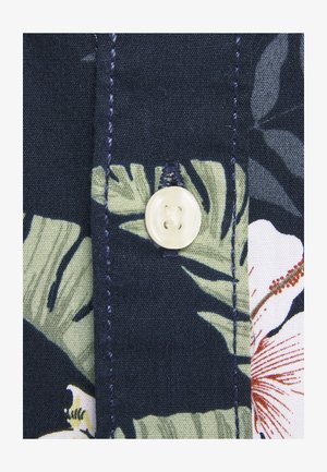 Tissu à motifs floraux présentant des feuilles vertes et des fleurs blanches sur un fond bleu marine, avec un bouton rond blanc et des coutures sombres contrastantes.