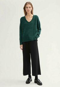 Roheline soonikkoes V-kaelusega kampsun ja soonikkoes servaga, kombineeritud mustade laia jalaga pükstega. Modell kannab musti pahkluu saapaid.