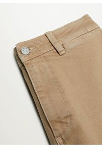 Pantalons en denim beige pliés, montrant un bouton avec le texte "King Jeans", une passant de ceinture, une poche latérale et des coutures doubles sur un fond clair.