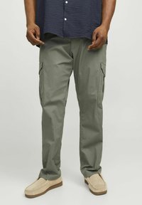 Cargo-Hosen in Olivgrün, mit seitlichen Taschen, geradem Schnitt und leichtem Stoff. Kombiniert mit beigen Slippern.