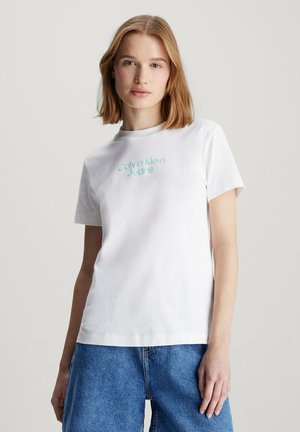 Camiseta de algodón blanca de manga corta, con un logo bordado en azul claro de "Calvin Klein Jeans" en el pecho. Diseño simple y clásico.
