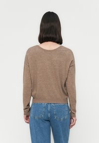 Maglione marrone in morbido knit con scollatura rotonda e maniche lunghe. Abbinato a jeans in denim blu a vita alta con un taglio classico e tasche.