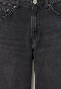 Close-up van de voorkant van zwarte spijkerbroek, met zicht op de knoop, ritssluiting, ceintuurlussen en voorzakken met metalen klinknagels.