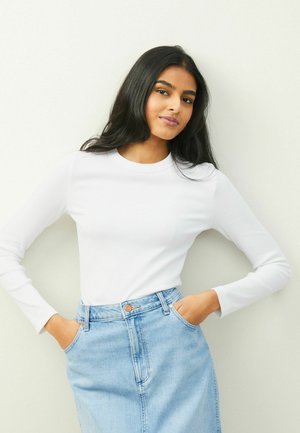Witte lange mouwen ribgebreide top gecombineerd met een lichtblauwe denim rok. De rok heeft een sluiting met knopen aan de voorkant en zakken.