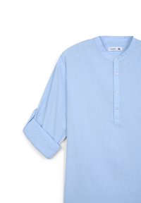 Camicia azzurro chiaro con colletto, chiusura con bottoni frontale, maniche arrotolate e una texture liscia. Presenta cinque bottoni per la chiusura.