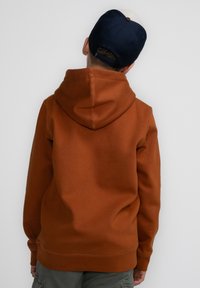 Verbrande oranjerode hoodie met een grote capuchon, ribgebreide manchetten en zoom. De achterkant toont een gladde textuur en minimale stikdetails.
