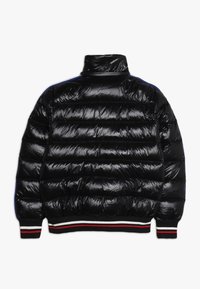 Doudoune noire avec col montant, présentant des sections matelassées horizontales, des accents bleus contrastants et un ourlet côtelé avec des rayures rouges et blanches.