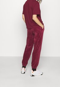 Pantalon en velours côtelé bordeaux avec poignets élastiques, assorti à un haut à manches courtes de la même couleur. Chaussures avec des accents blancs et orange.