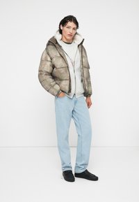 Olíva zöld és szürke mintás steppelt dzseki, bélelt kapucnival, szürke pulóverrel és világoskék farmernadrággal párosítva. Fekete cipő.