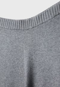 Gros plan sur une ceinture en maille côtelée grise sur un pantalon en tissu doux avec une couture avant visible et un matériau texturé.