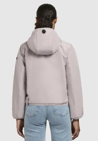 Light lavender puffer jacket with a hood, elastic cuffs, and a smooth texture. Features a circular logo on the back and side pocket.