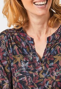 Florale Bluse mit dunklem Hintergrund und mehrfarbigen Blättermustern. Weicher Stoff, V-Ausschnitt-Design und geraffteDetails an den Schultern.