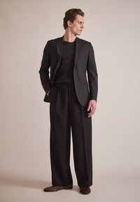 Traje negro ajustado con una chaqueta de corte slim y pantalones de pierna ancha. Camisa negra texturizada debajo. El calzado presenta un diseño de estampado de leopardo.