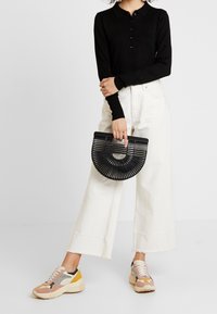 Zwart gebreid poloshirt, brede witte spijkerbroek, zwarte halve maan handtas en meerkleurige chunky sneakers met afgeronde zolen.