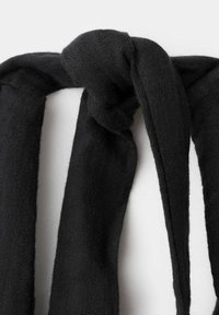 Écharpe noire tricotée nouée en un nœud lâche sur fond blanc uni, montrant la texture et les détails du tissu.