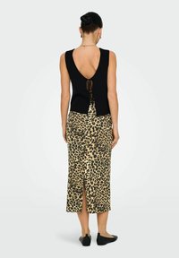 Zwarte geribbelde tanktop met een lage rug en strikdetail, gecombineerd met een midi-skirt met luipaardprint, voorzien van een zijsplit en een gladde textuur.