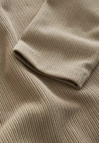 Material bej cu dungi, având o textură netedă, care prezintă o margine de mânecă pliată. Materialul are linii verticale și o strălucire subtilă.