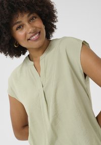 Top verde chiaro a maniche corte con scollatura a V e tessuto testurizzato. Presenta sottili righe verticali e una vestibilità rilassata.