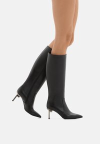 Stivali neri in pelle al ginocchio con punte appuntite e tacchi a stiletto metallici. Texture liscia, cuciture minime e design elegante.