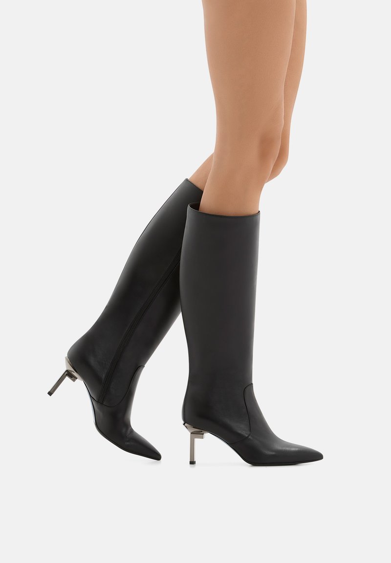 Stivali neri in pelle al ginocchio con punte appuntite e tacchi a stiletto metallici. Texture liscia, cuciture minime e design elegante.