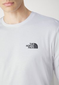 Hvid bomulds t-shirt med rund halsudskæring, der har et lille sort logo af "The North Face" på venstre side af brystet.