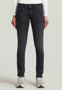 Slim-fit donkergrijze jeans van denim, met een knoopsluiting, voorzakken en een gladde textuur. Gecombineerd met grijze sneakers.