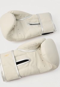 Μπεζ γάντια πυγμαχίας με ασημί λεπτομέρειες, κατασκευασμένα από συνθετικό υλικό. Διαθέτουν οπές αερισμού και ισχυρούς ιμάντες στον καρπό για υποστήριξη.