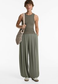Canotta a coste verde oliva abbinata a pantaloni a gamba larga nella stessa tonalità, completata da una borsa all'uncinetto e sneakers grigie.