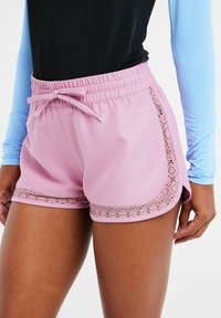 Shorts sportivi rosa chiaro con vita elastica, cordoncino decorativo e pizzo sui lati; tessuto liscio con una vestibilità comoda.