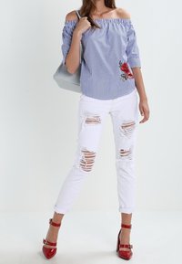 Blusa a spalle scoperte a righe blu e bianche, con ricami floreali; abbinata a jeans skinny bianchi strappati e scarpe con tacco rosse.