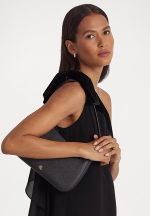 Bolso estructurado negro con un acabado texturizado, que presenta una forma curva y una correa delgada, sostenido contra un vestido negro con un cuello de terciopelo.