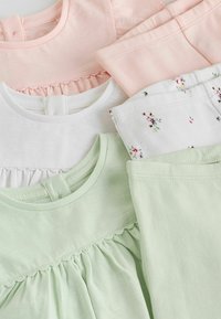 Trois hauts pour bébé en rose pastel, blanc et vert avec des détails à volants et des pantalons assortis, y compris des pantalons blancs avec de petits imprimés floraux.