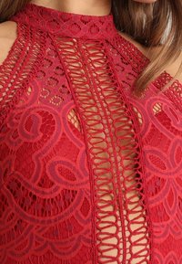 Rotes Spitzenoberteil mit aufwendigen floralen Mustern und Ausschnitten, einem hohen Kragen und strukturiertem Saum.