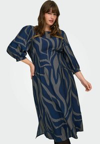 Vestido midi azul marino con mangas abullonadas, que presenta patrones de rayas doradas onduladas. Tejido ligero con un corte relajado y aberturas laterales en el dobladillo.